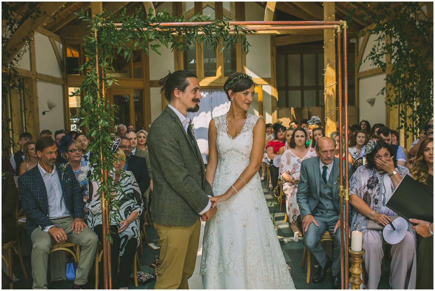 Bride and Groom stand hand in hand under copper pipe arch way