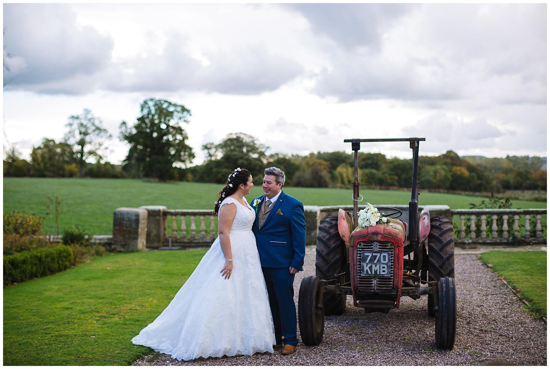 Wedding photography at Willington Hall bride and groom stand by tractor