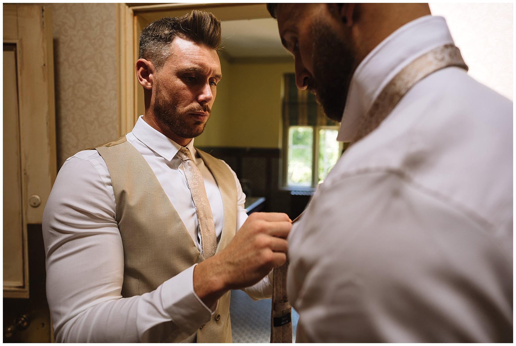 groom helps groomsman fasten his tie