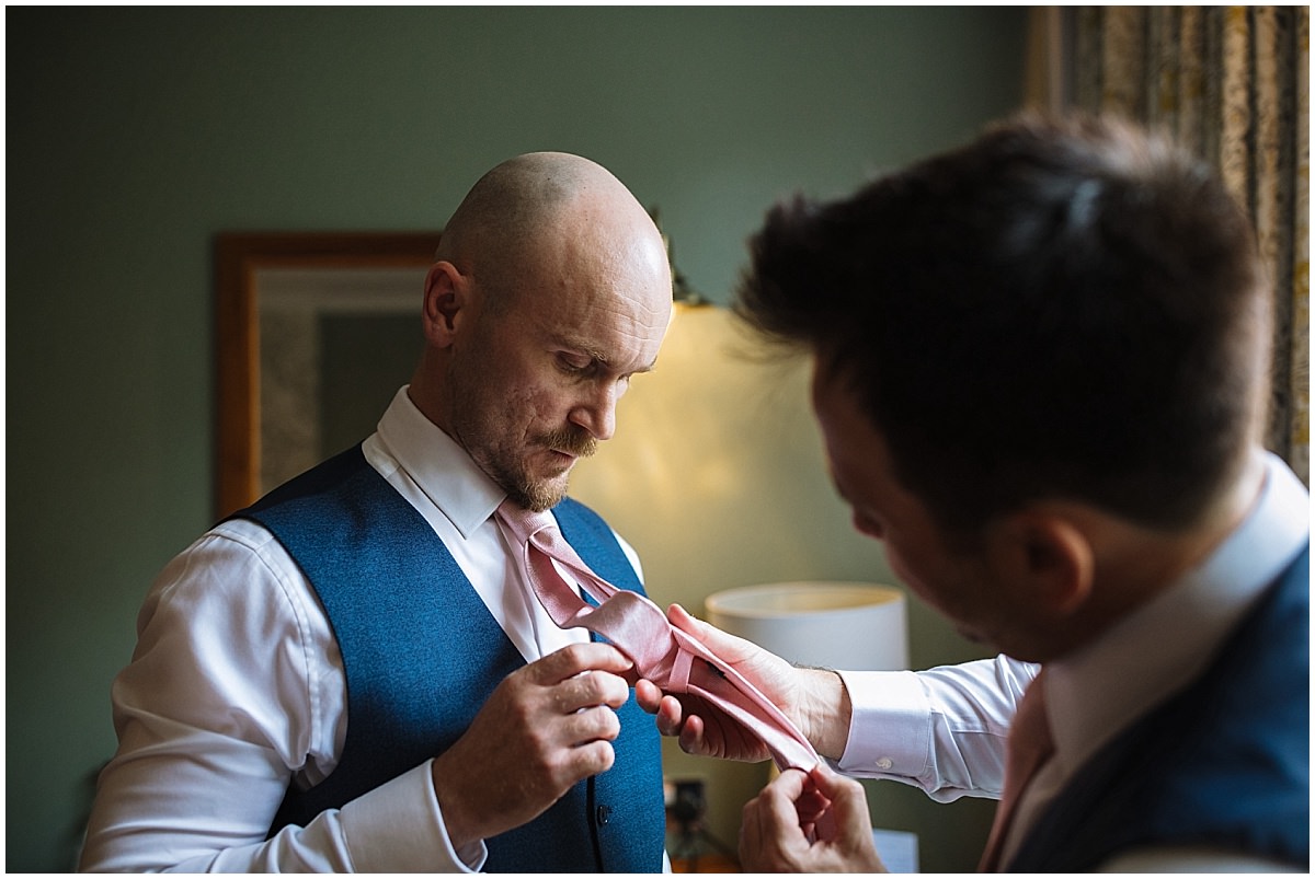 Groom helps best man tie his tie before the wedding