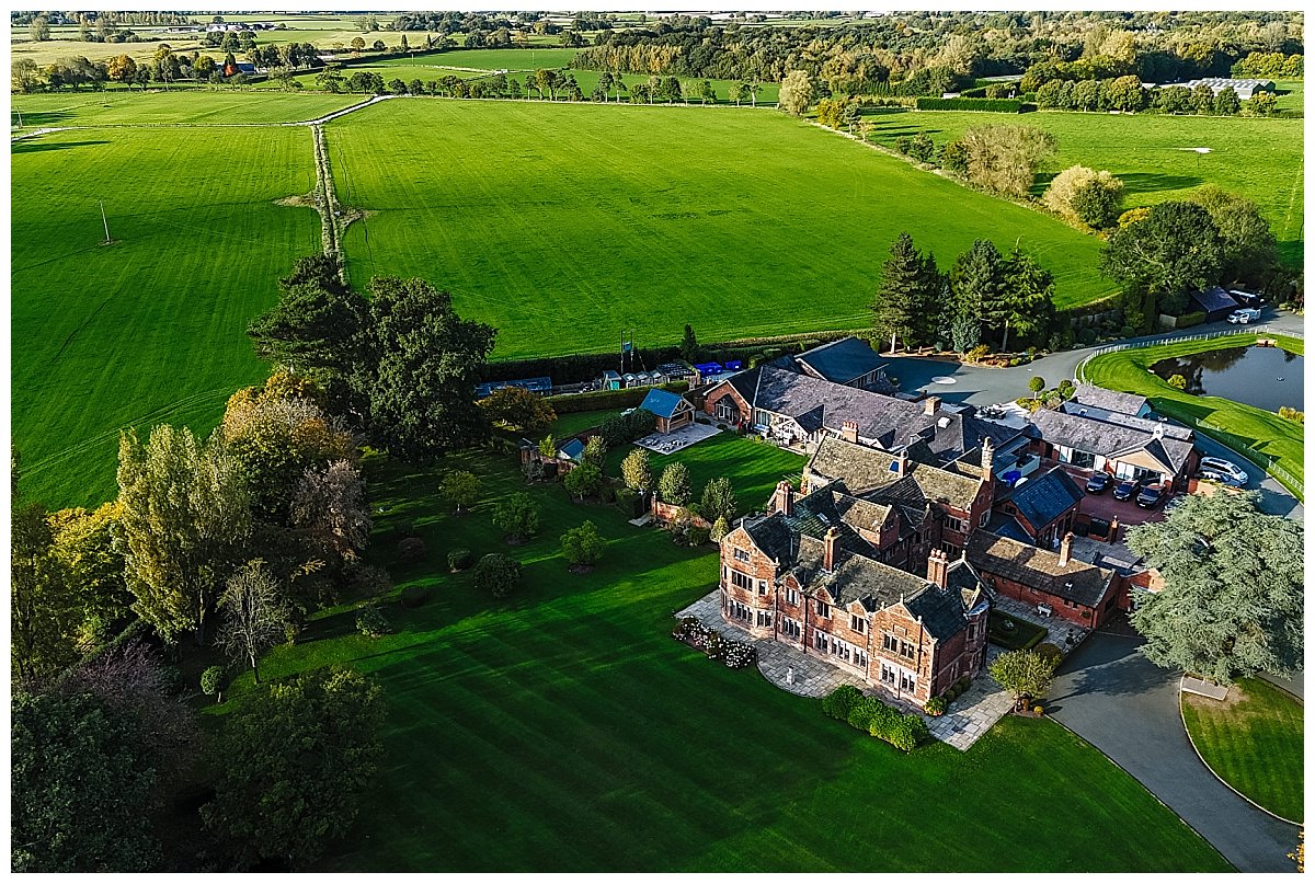 Aerial view of Colshaw Hall with manicured gardens, surrounded by expansive green fields and trees.