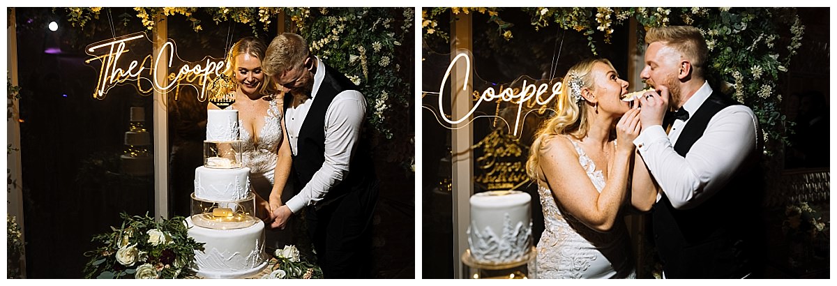 A joyful couple shares a moment while cutting their wedding cake, with a glowing sign reading "The Coopers" in the background, surrounded by floral decorations.