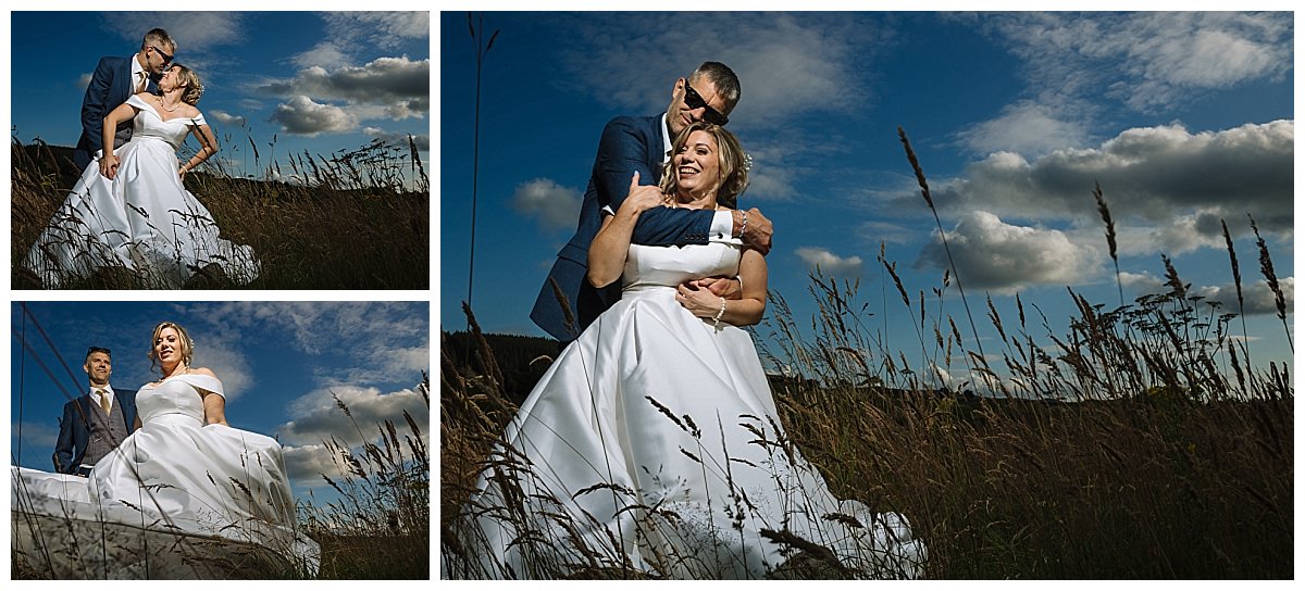 A joyful couple in wedding attire, embracing in a scenic field under a dramatic sky filled with clouds.