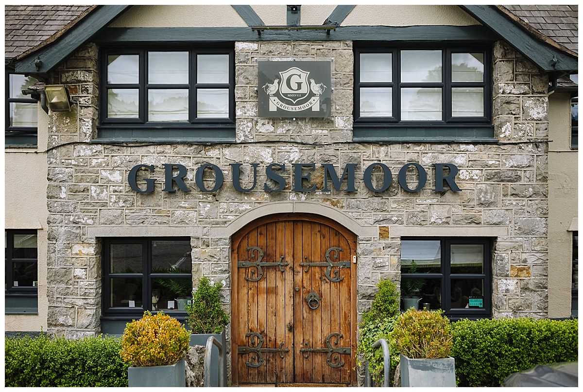 Front entrance and signage of Grousemoor, featuring a rustic wooden door and stone facade.