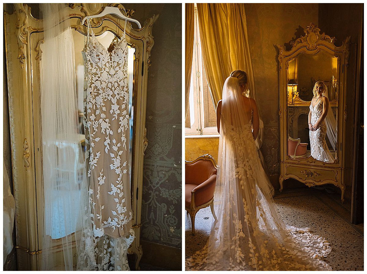 A stunning wedding dress adorned with intricate white floral designs hangs on a vintage mirror, reflecting a bride in her bridal veil and gown, captured in a beautifully lit room at Palazzo Parisio in Naxxar.