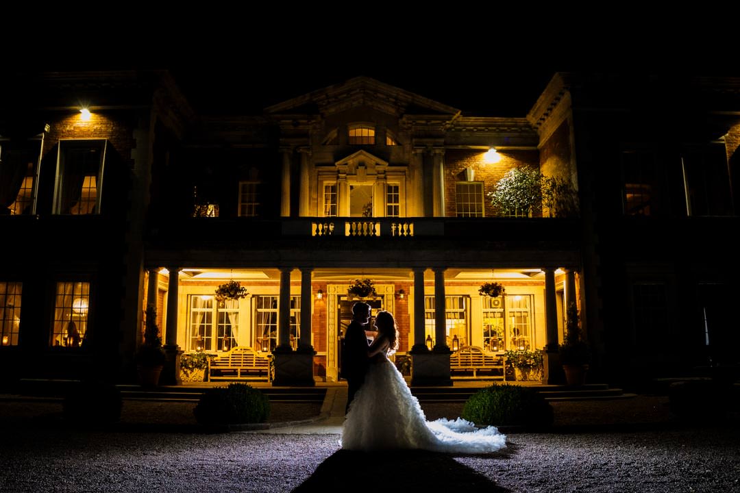 A couple in formal attire sharing a moment in front of a beautifully lit historic building at night.