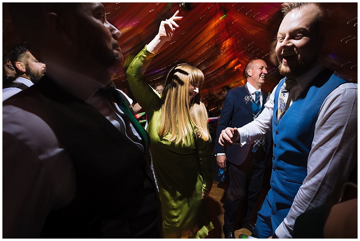 A lively scene of people enjoying a dance party, featuring a woman in a green dress raising her hand joyfully amidst a vibrant atmosphere.