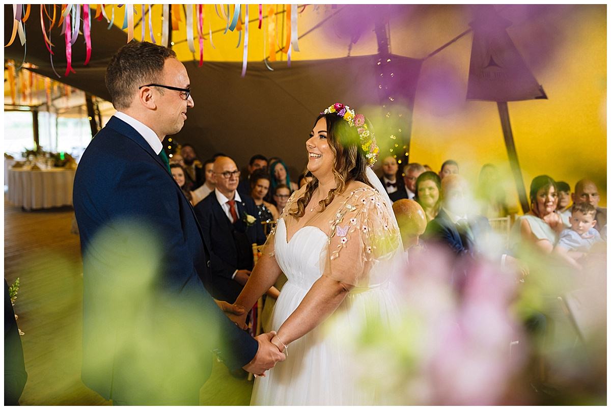 A joyful couple exchanges vows at their wedding ceremony, surrounded by family and friends in a vibrant, decorated venue.