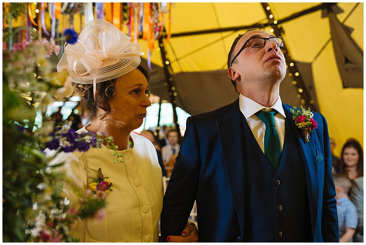 A man and a woman share a heartfelt moment during a wedding ceremony, surrounded by floral decorations and a lively atmosphere.