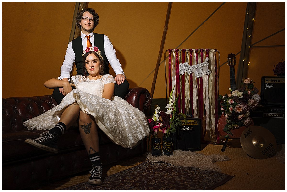 A couple poses gracefully on a vintage sofa in a whimsical tent, surrounded by floral arrangements and decorative elements that exude a joyous atmosphere.