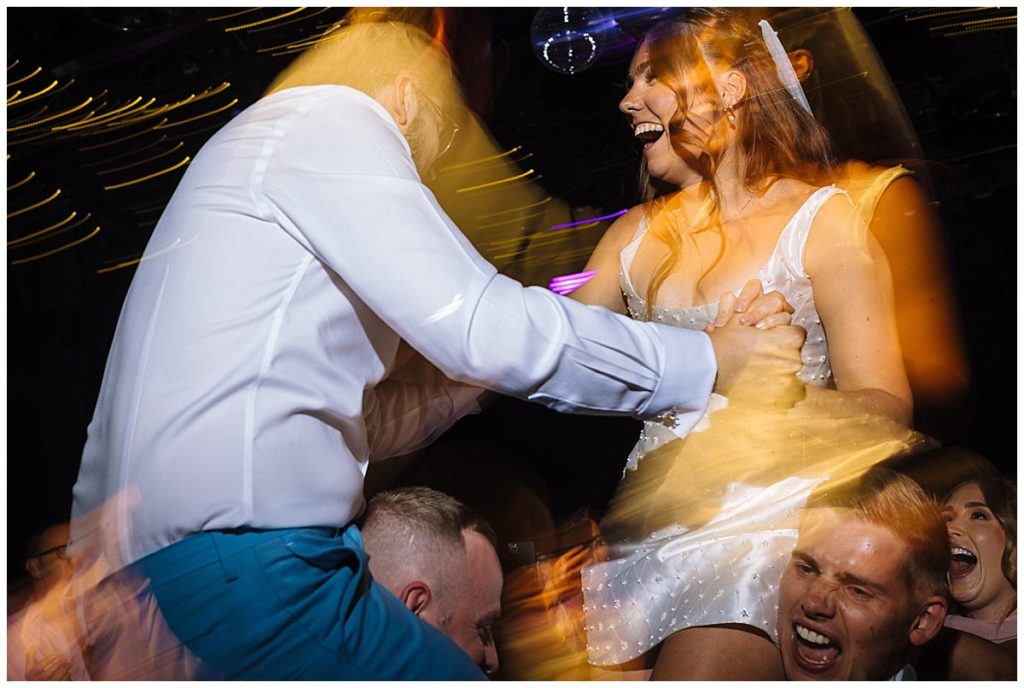 A lively dance scene featuring a woman in a white dress joyfully interacting with a man while other guests celebrate in the background, capturing the energy of the moment.
