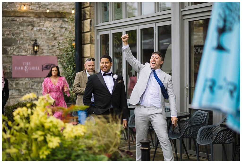A joyful gathering outside a venue, featuring two well-dressed men celebrating, with others in the background enjoying the atmosphere.