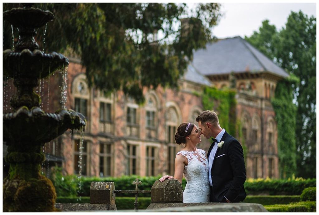 A bride and groom share a tender moment by a fountain at a weekday wedding at soughton hall