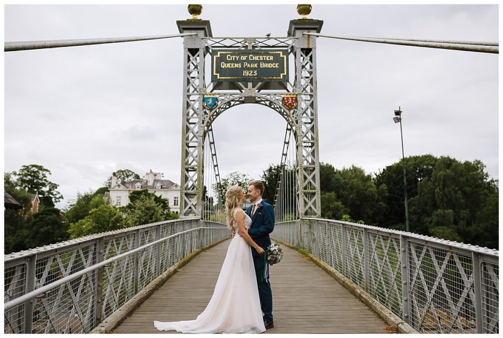 A joyful couple stands on Queens Park Bridge in Chester at a weekday wedding