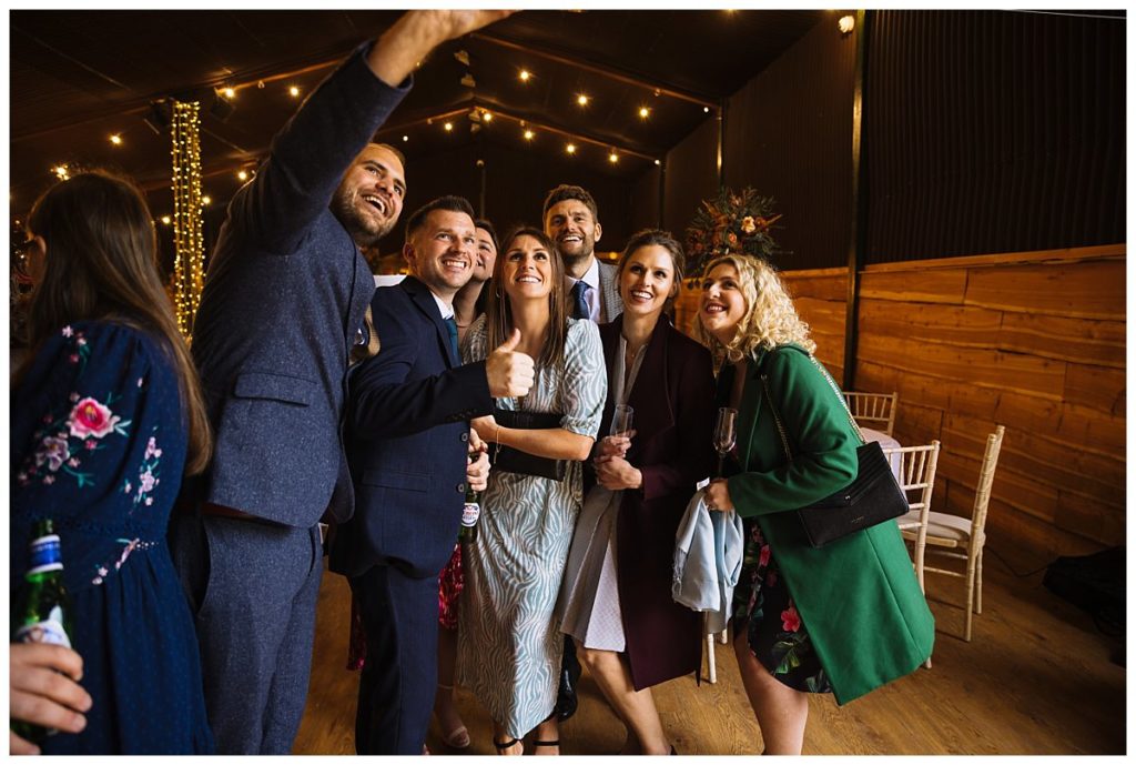 A cheerful group of friends taking a selfie at a festive gathering, indoors with warm lighting and wooden decor.