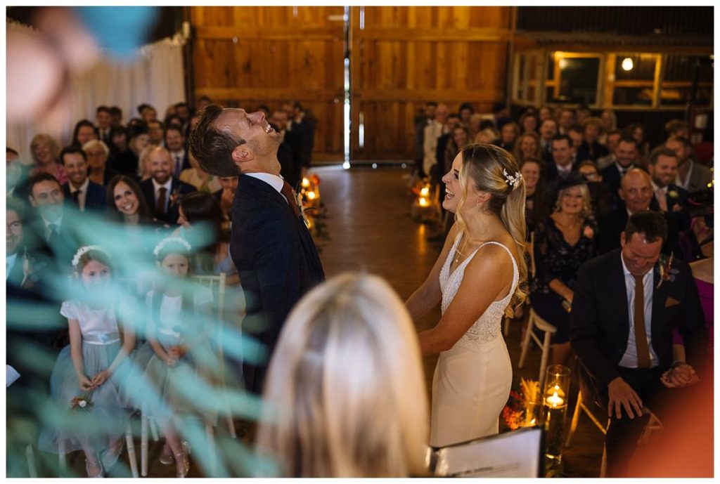 A couple shares a heartfelt moment during their wedding ceremony, surrounded by a joyful audience in a beautifully decorated barn setting.