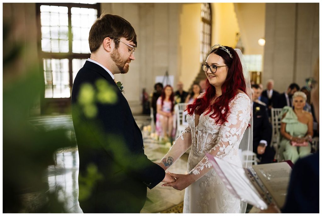 A couple exchanges vows during a wedding ceremony, surrounded by guests in a beautifully decorated venue.