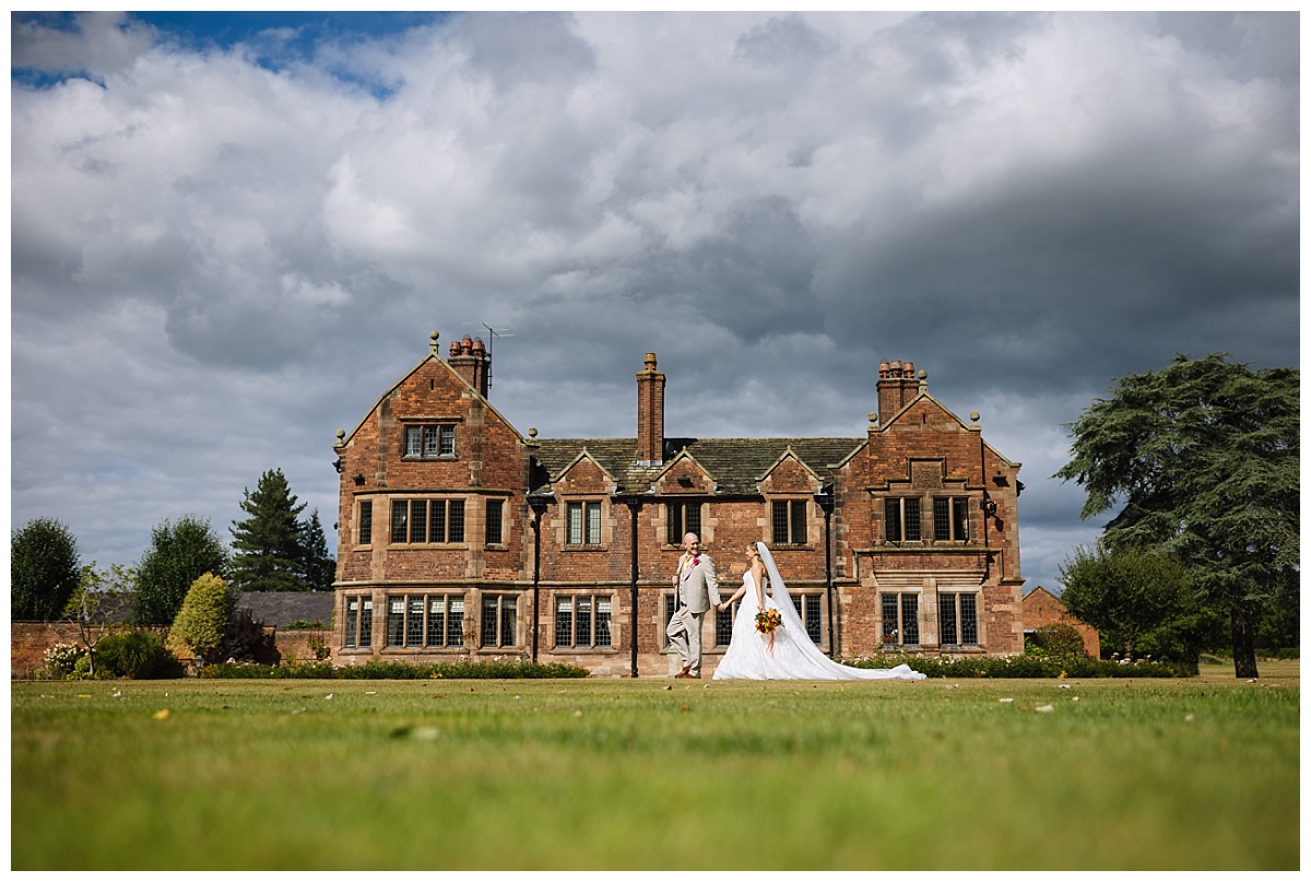 a couple walk hand in hand across the lawns of colshaw hall on their wedding day